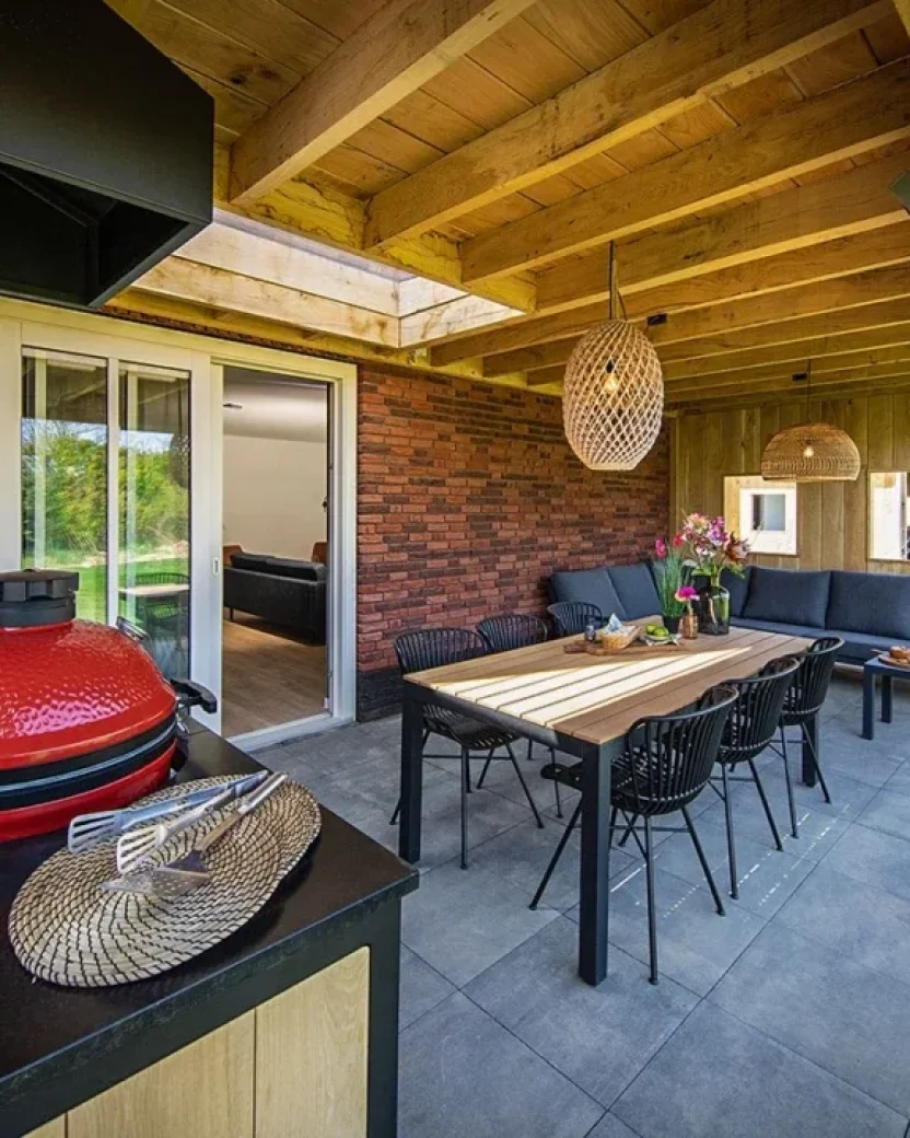 Overdekt terras met eettafel, loungehoek en barbecue bij een vakantieverblijf.