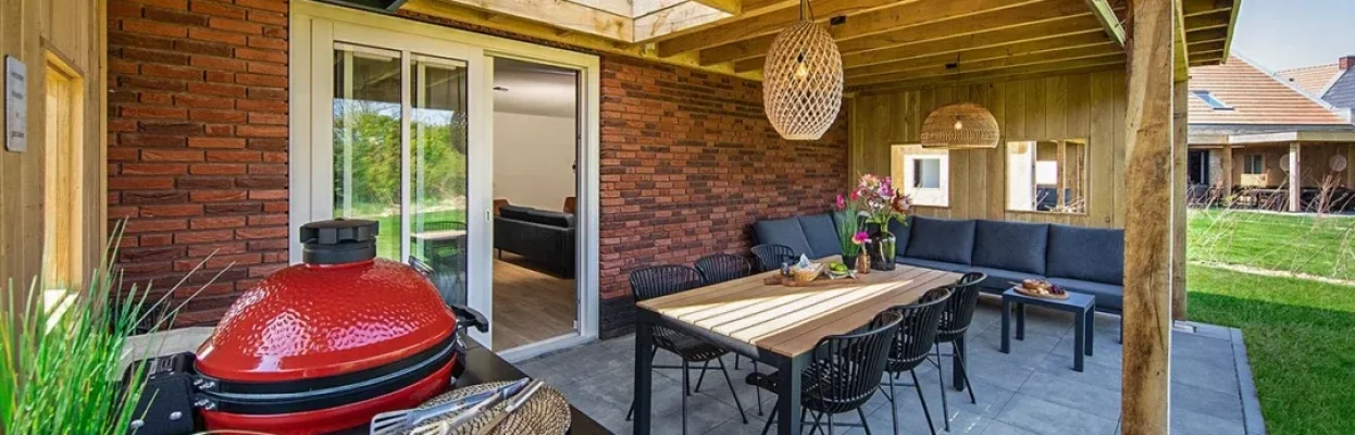 Overdekt terras met eettafel, loungehoek en barbecue bij een vakantieverblijf.