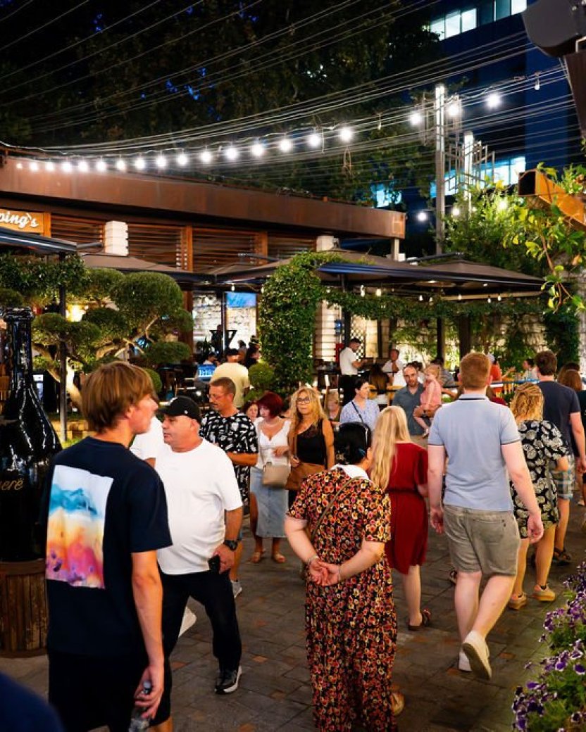 Reisgenoten wandelen samen door een levendige straat met restaurants en terrassen in de avond.