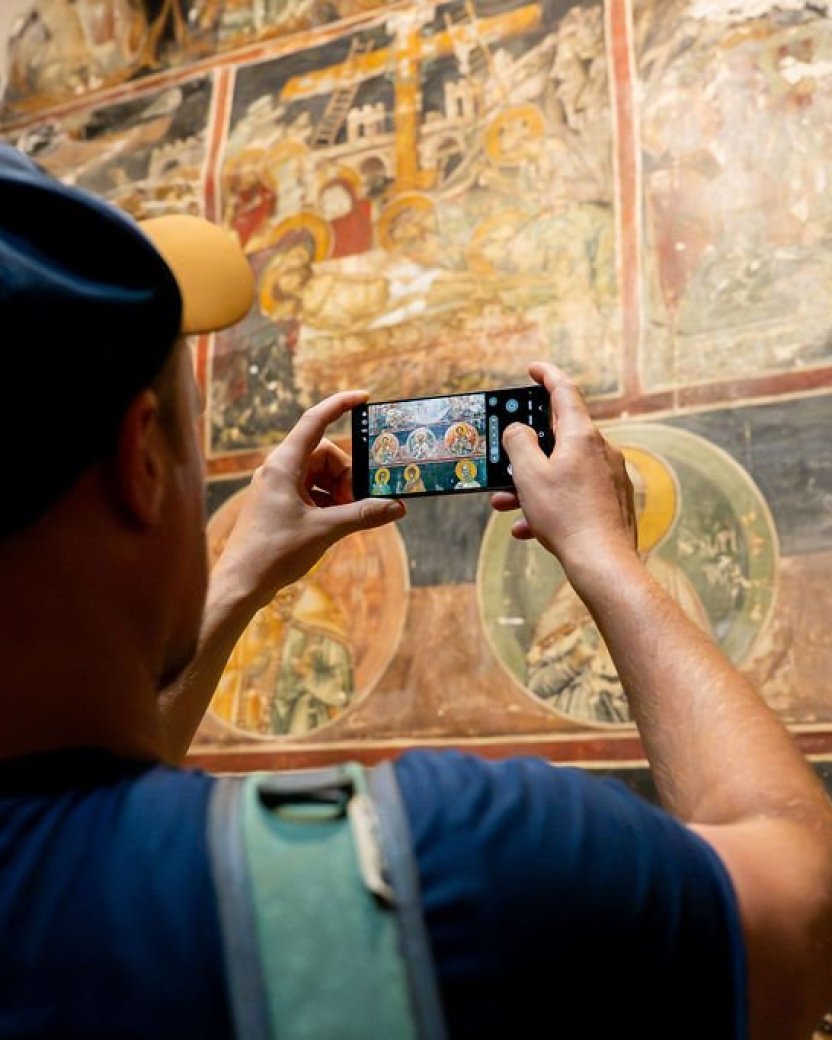 Reisgenoot maakt een foto van historische muurschilderingen tijdens een cultureel bezoek.