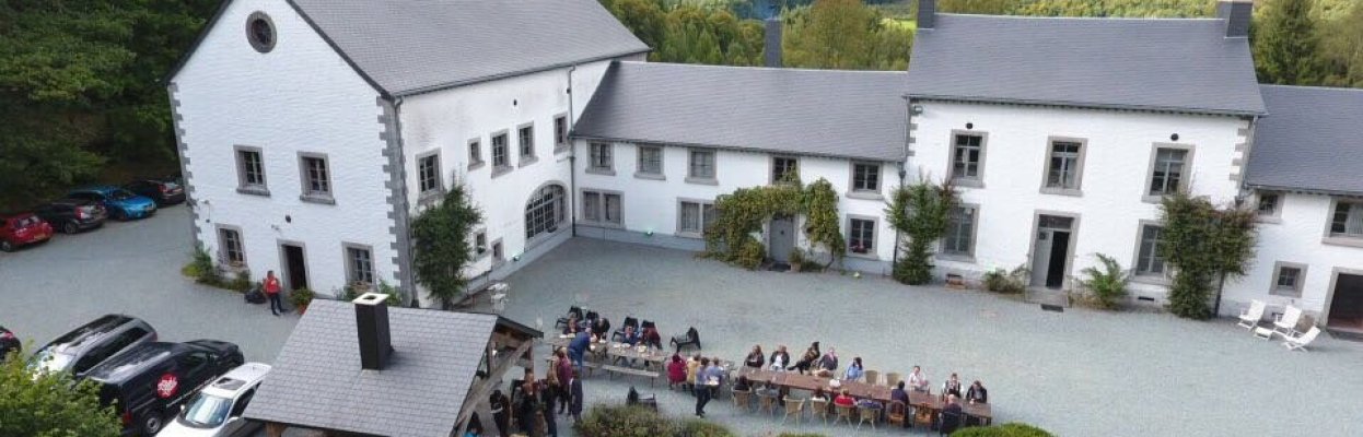 Groep reisgenoten zit samen buiten aan lange tafels bij een groot landhuis in de Ardennen.