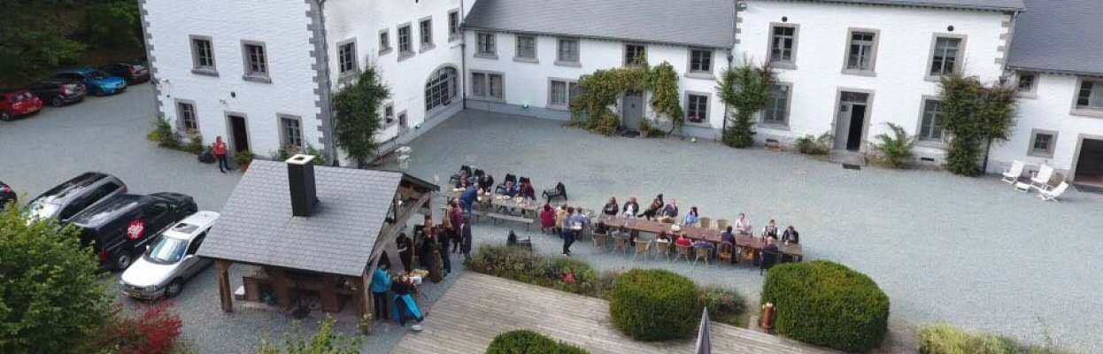 Groep reisgenoten zit samen buiten aan lange tafels bij een groot landhuis in de Ardennen.