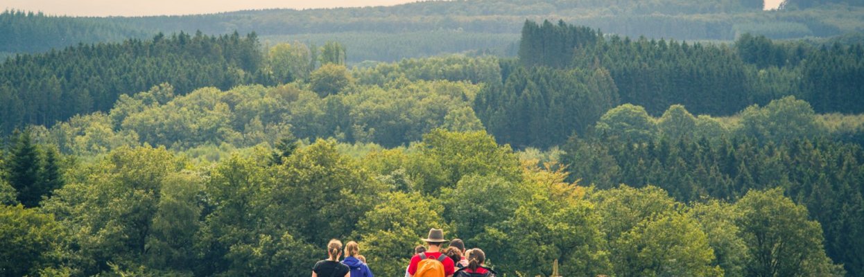 Groep reisgenoten wandelt samen over een landelijk pad met uitzicht op de groene heuvels van de Ardennen.