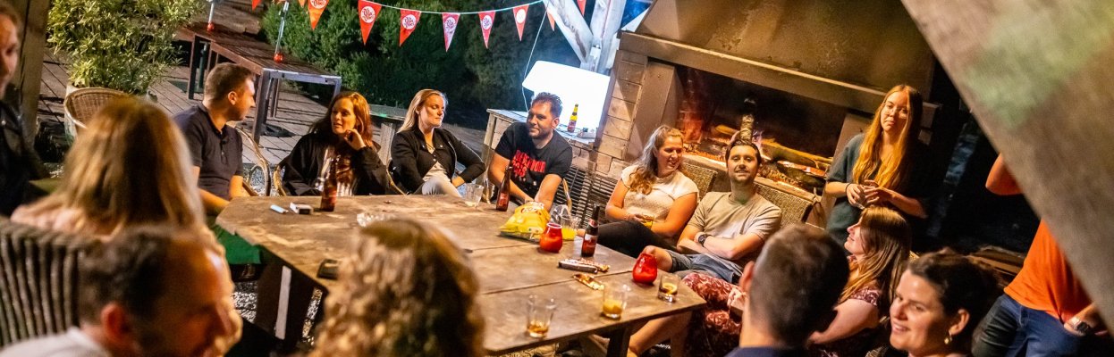 Groep reisgenoten zit samen rond een grote tafel bij de open haard tijdens een avond in de Ardennen.
