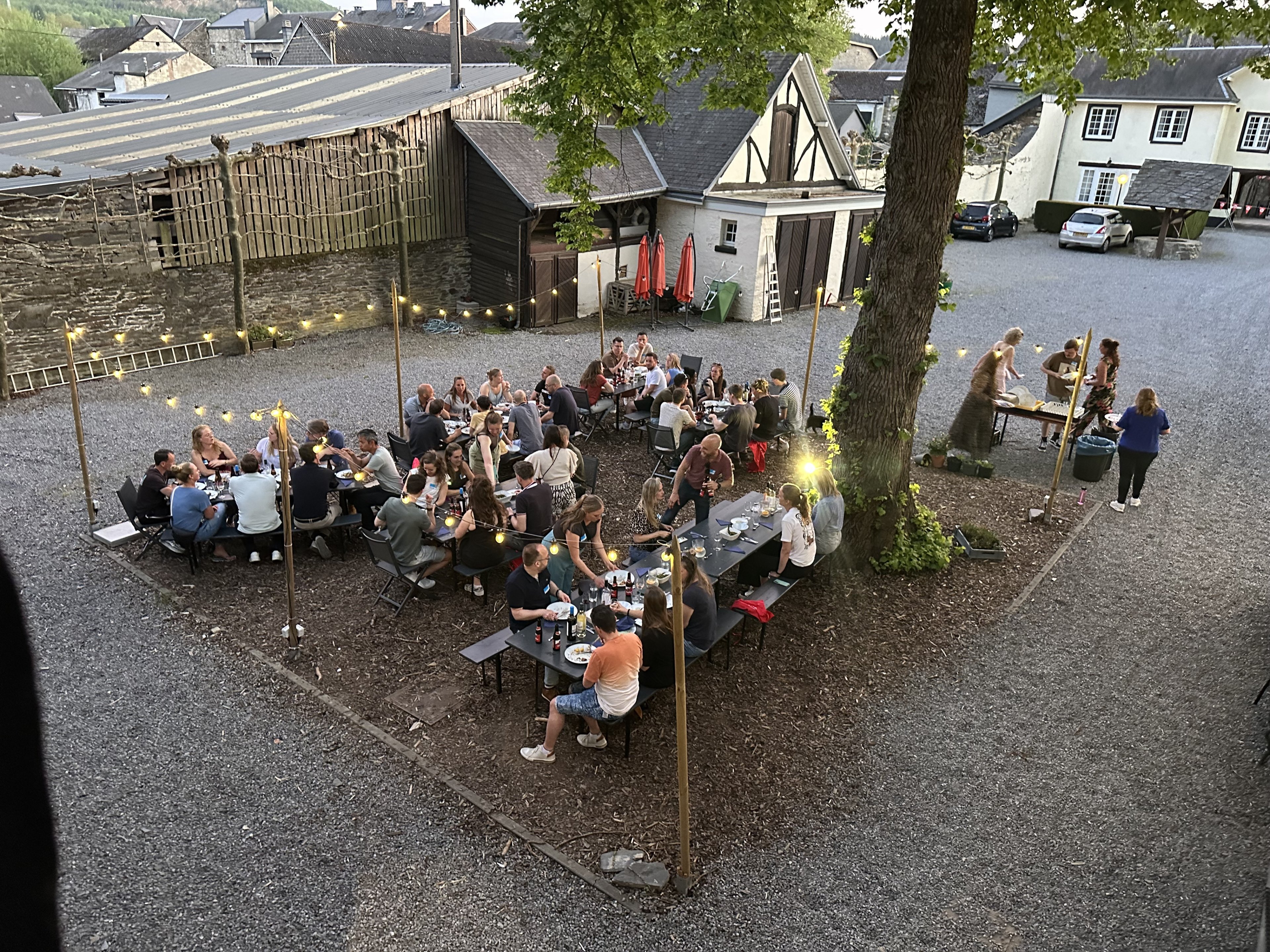 Groep reisgenoten eet samen buiten aan lange tafels op een sfeervol verlicht binnenplein.