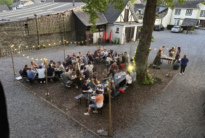 Groep reisgenoten eet samen buiten aan lange tafels op een sfeervol verlicht binnenplein.