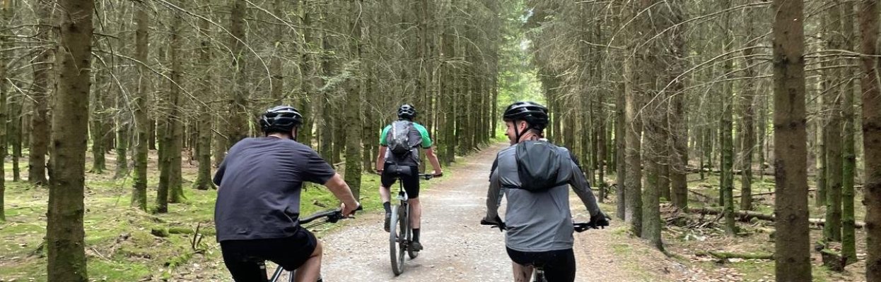 Drie reisgenoten fietsen samen over een bospad door de Ardennen.