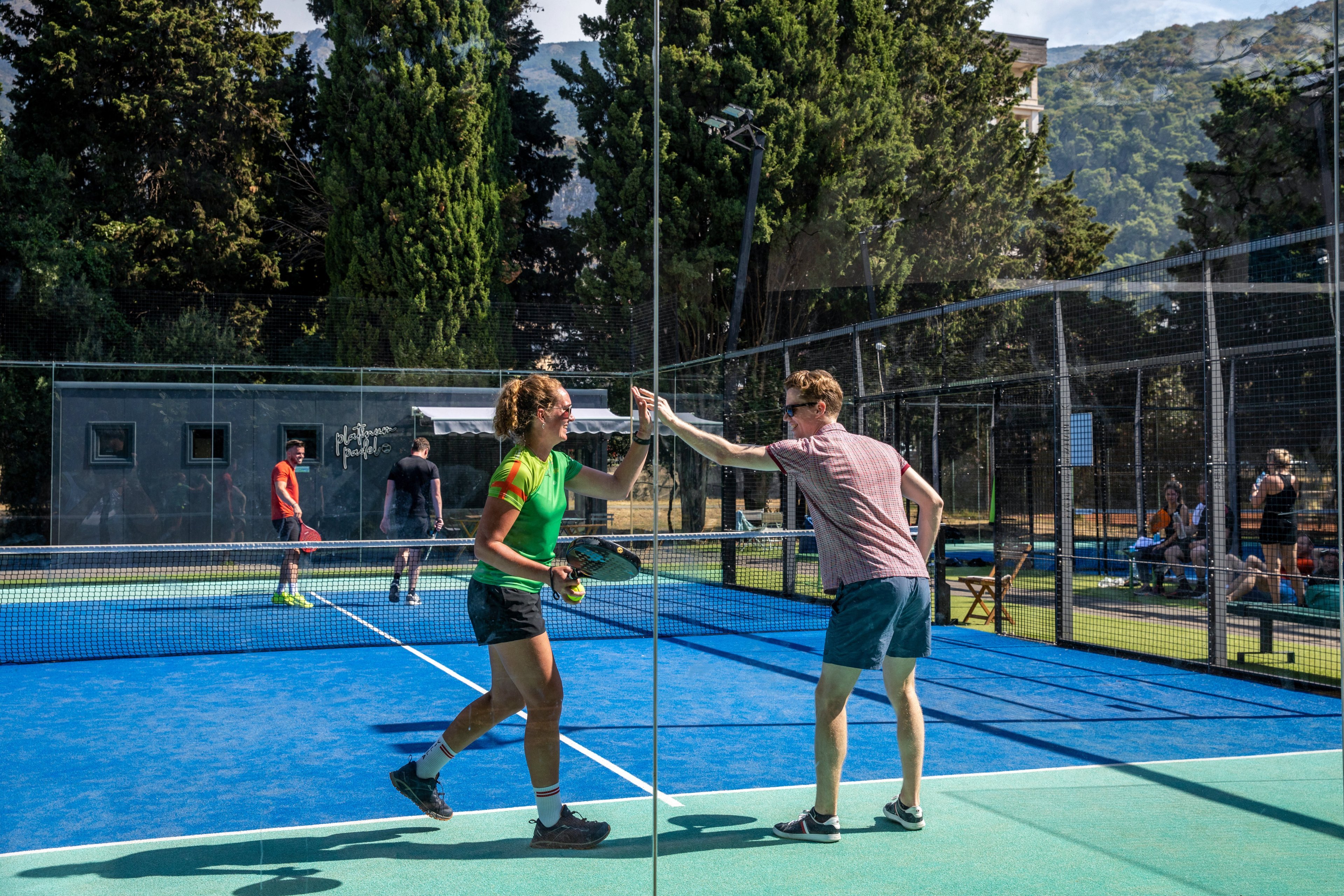 Padellers geven elkaar een high five na winst op de padelbaan.