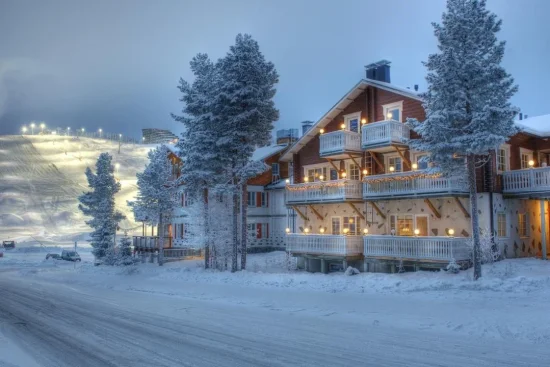 Sfeervol chalet in een besneeuwd winterdorp met verlichte skipiste op de achtergrond.