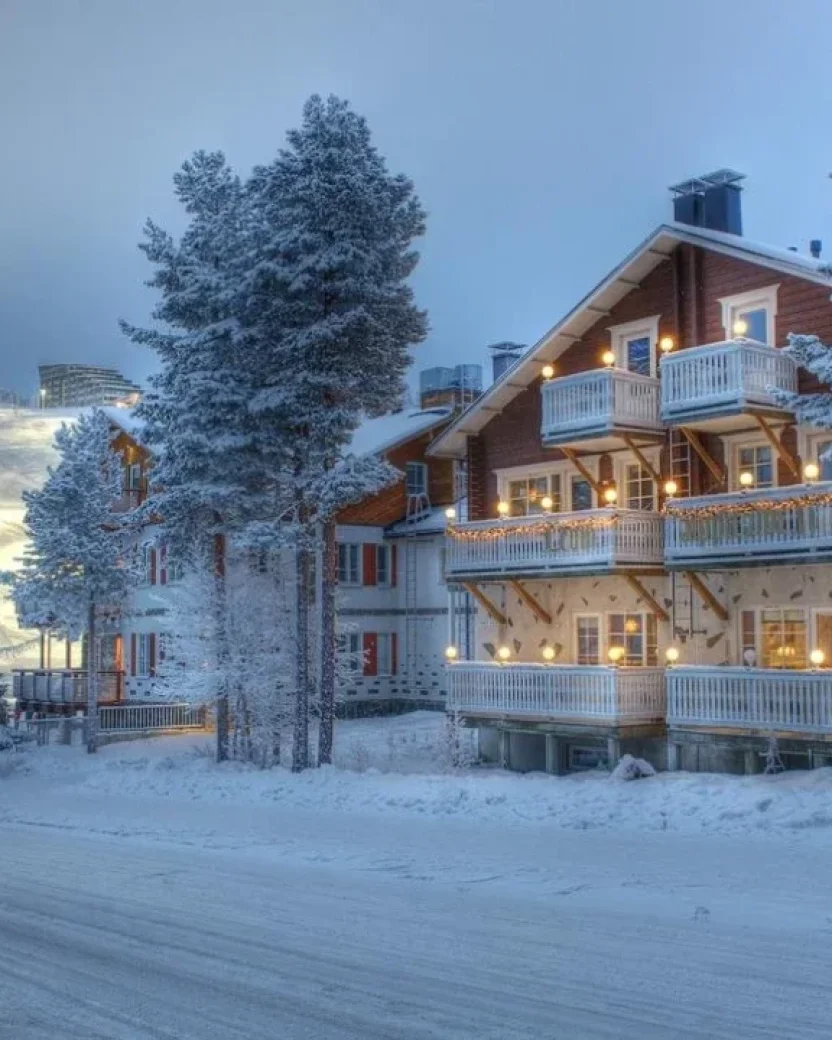 Sfeervol chalet in een besneeuwd winterdorp met verlichte skipiste op de achtergrond.