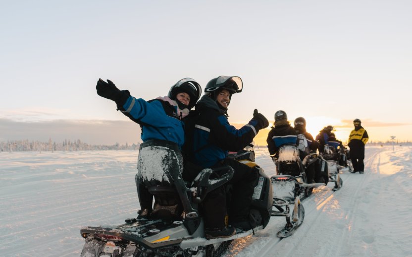 Reisgenoten rijden samen op sneeuwscooters door een besneeuwd winterlandschap.