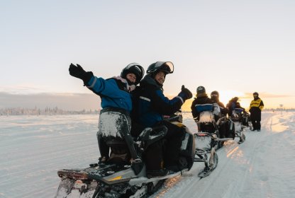 Reisgenoten rijden samen op sneeuwscooters door een besneeuwd winterlandschap.