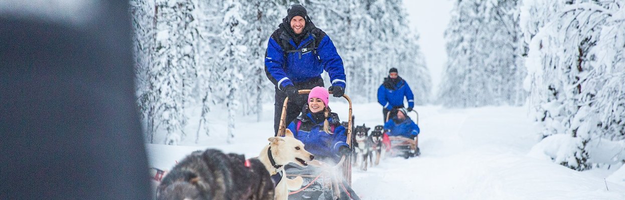 Reisgenoten maken samen een huskysledetocht door een besneeuwd bos.