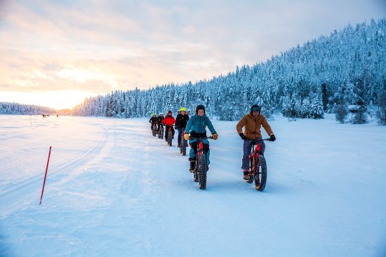 Groep reisgenoten fietst met fatbikes door een besneeuwd landschap bij zonsondergang.