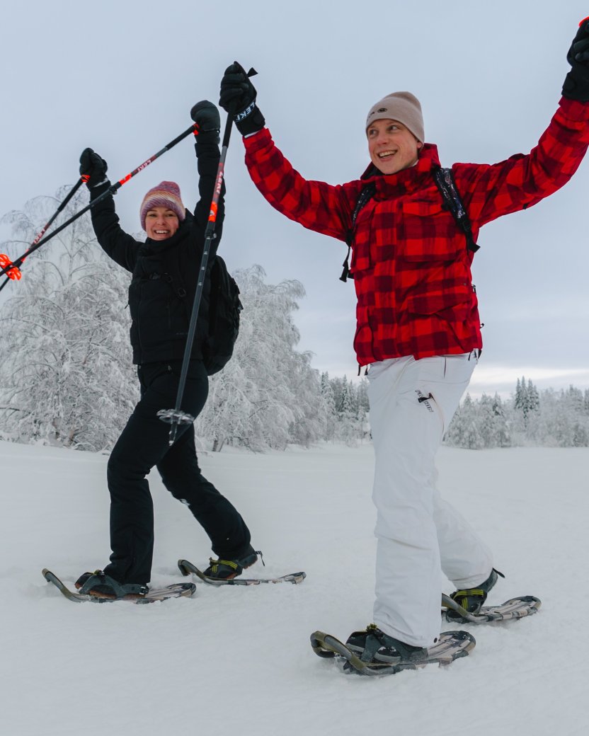 Twee reisgenoten lopen op sneeuwschoenen door een besneeuwd winterlandschap.