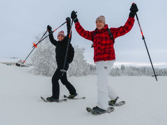 Twee reisgenoten lopen op sneeuwschoenen door een besneeuwd winterlandschap.