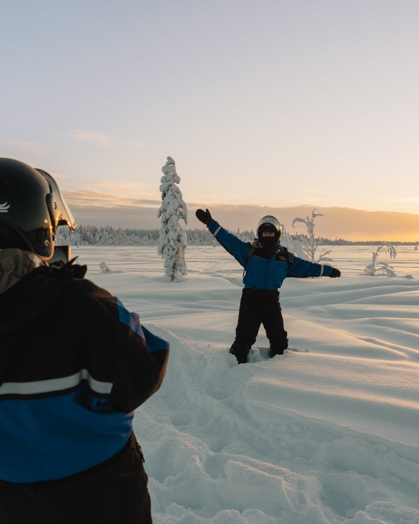 Reisgenoot poseert in de diepe sneeuw bij zonsondergang tijdens een winteractiviteit.