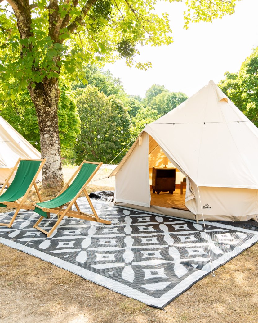 Glampingtenten met ligstoelen op een groene plek tussen de bomen.