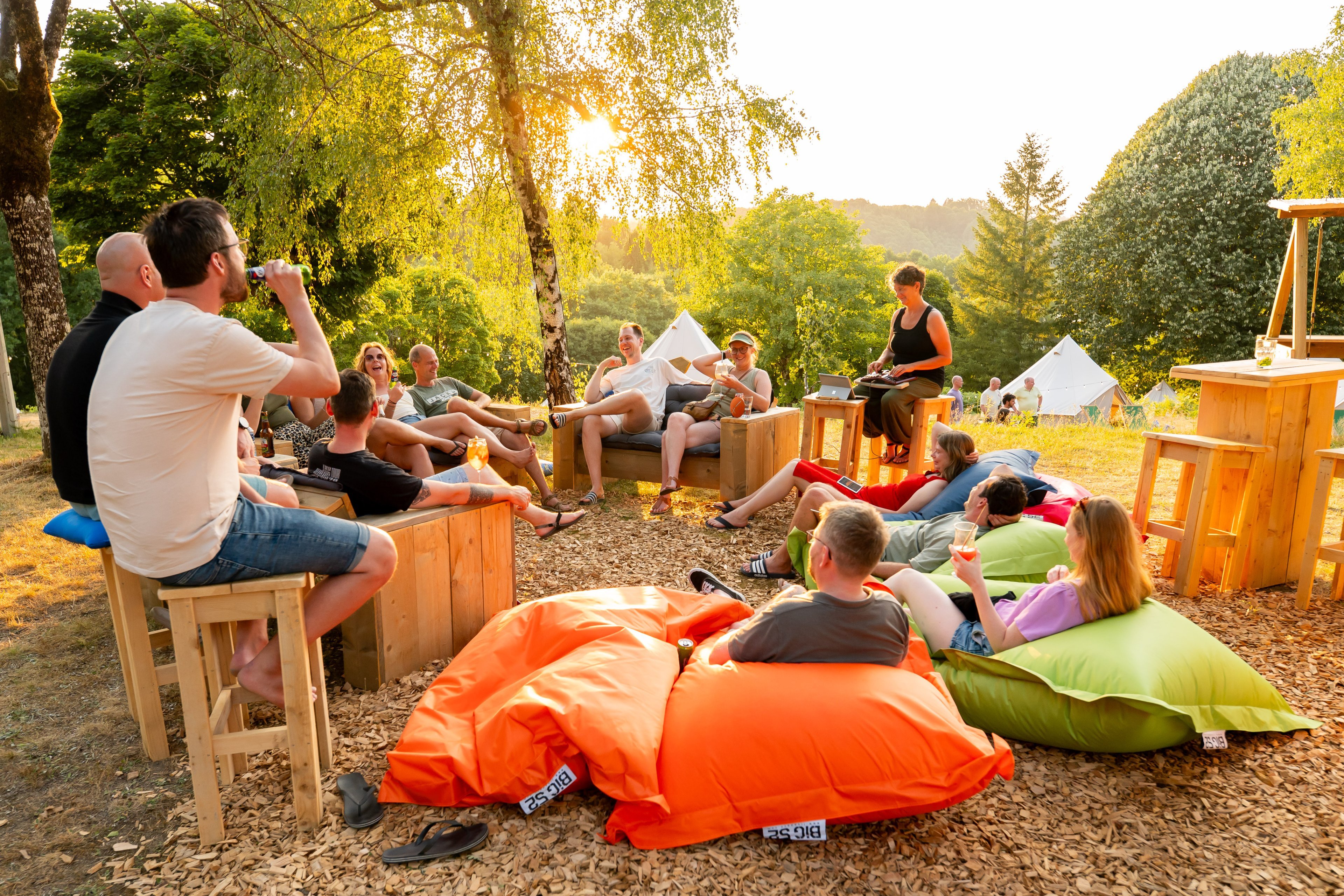 Groep reisgenoten ontspant samen op zitzakken en houten banken bij de glamping in de avondzon.