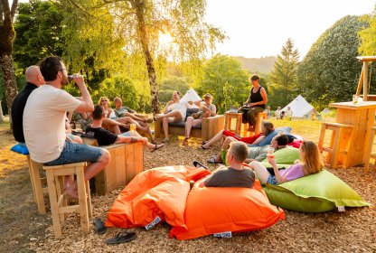 Groep reisgenoten ontspant samen op zitzakken en houten banken bij de glamping in de avondzon.