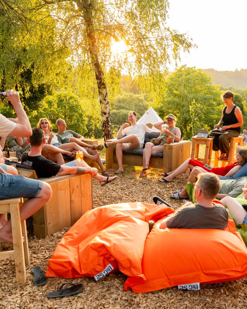 Groep reisgenoten ontspant samen op zitzakken en houten banken bij de glamping in de avondzon.