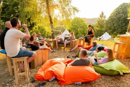Groep reisgenoten ontspant samen op zitzakken en houten banken bij de glamping in de avondzon.
