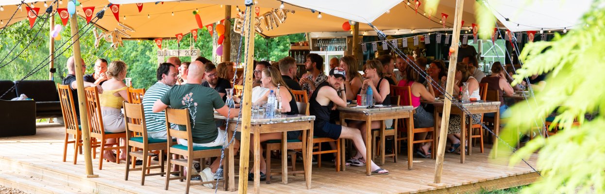 Groep reisgenoten zit samen aan tafels onder een grote tent op de glamping.