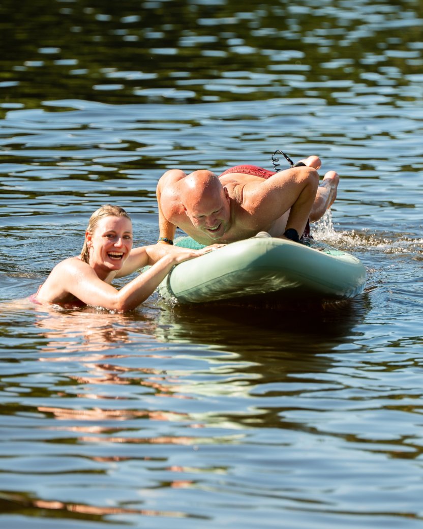 Twee reisgenoten zwemmen en spelen samen met een luchtbed in het meer.