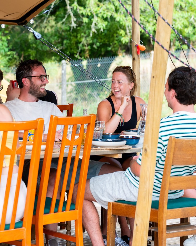 Reisgenoten zitten samen aan tafel en praten met elkaar tijdens een maaltijd op de glamping.
