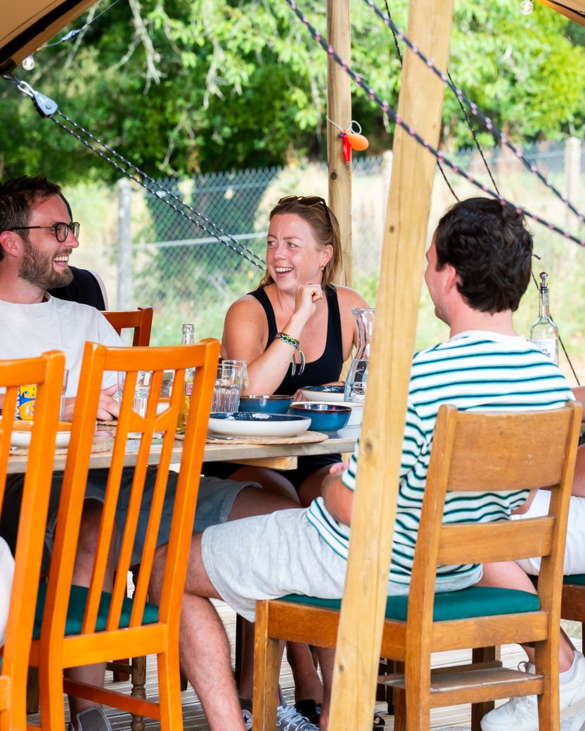 Reisgenoten zitten samen aan tafel en praten met elkaar tijdens een maaltijd op de glamping.
