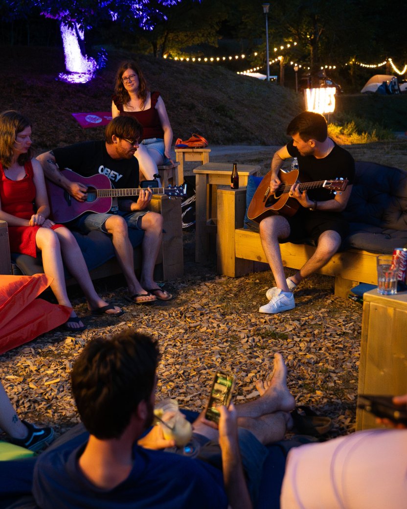 Reisgenoten luisteren samen naar live gitaarmuziek tijdens een sfeervolle avond op de glamping.