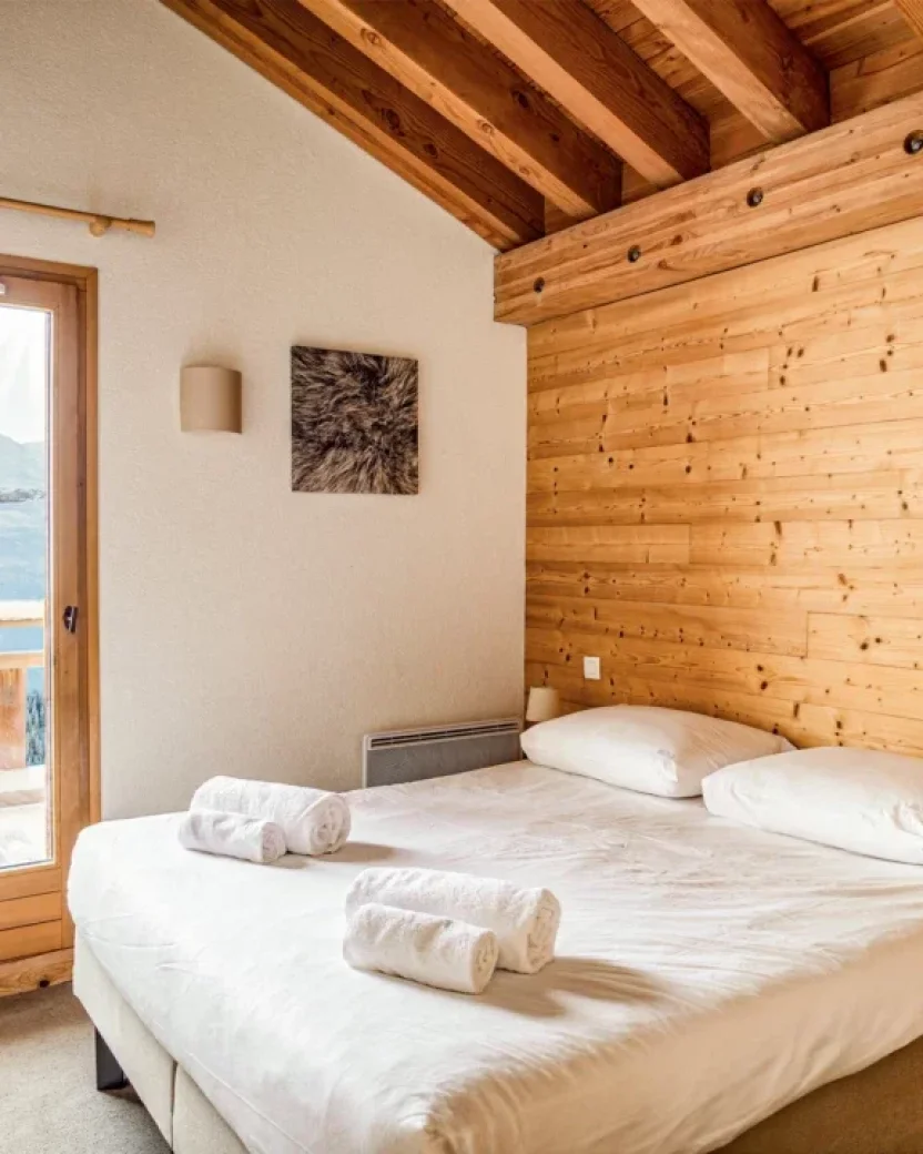 Ruime slaapkamer met houten details en uitzicht op de besneeuwde bergen.