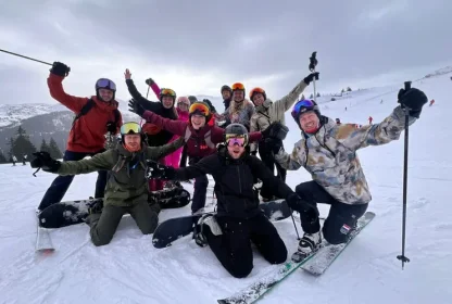 Groep skiërs en snowboarders poseert enthousiast samen op de piste.
