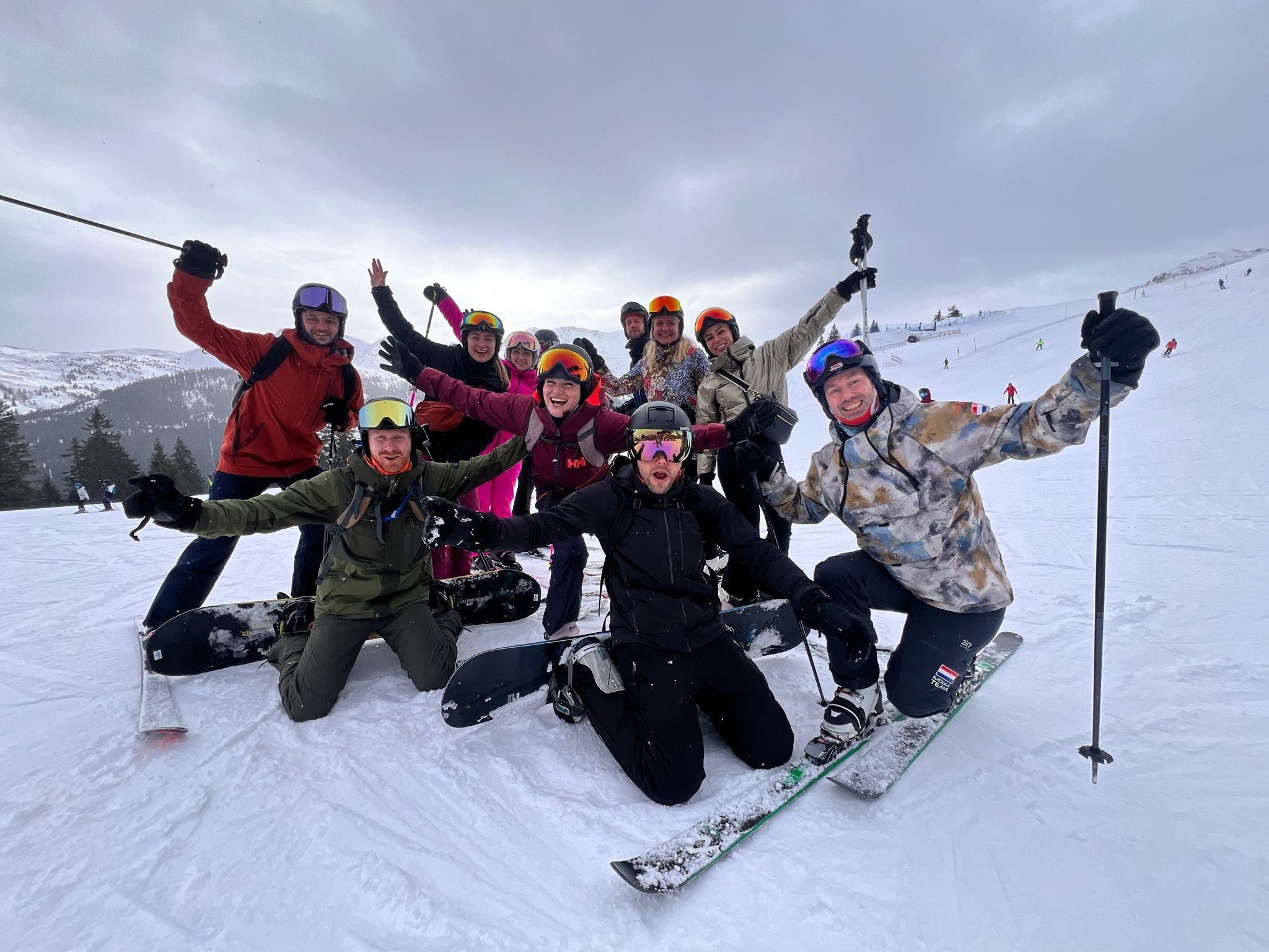Groep skiërs en snowboarders poseert enthousiast samen op de piste.