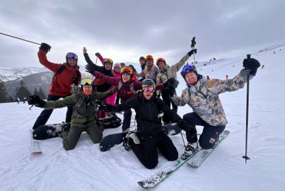 Groep skiërs en snowboarders poseert enthousiast samen op de piste.