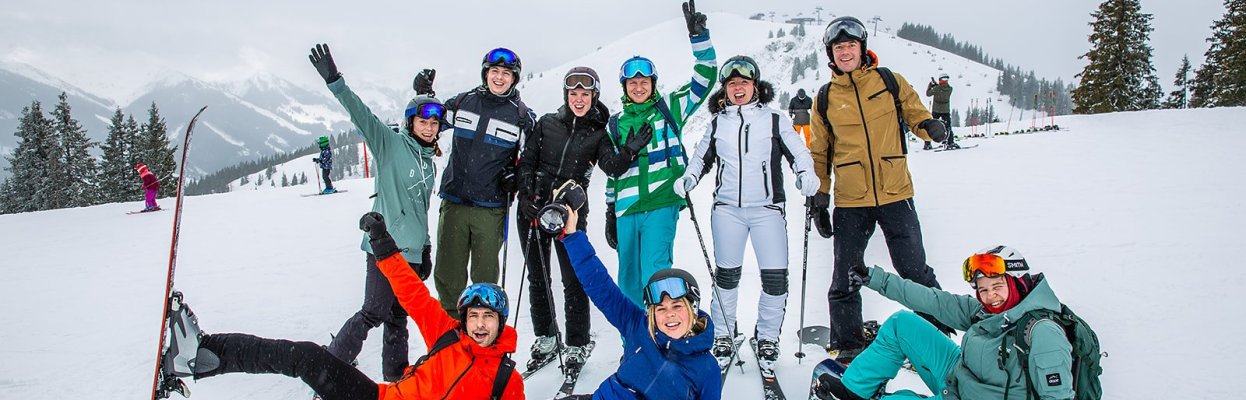 Groep skiërs en snowboarders poseert samen op een besneeuwde piste.