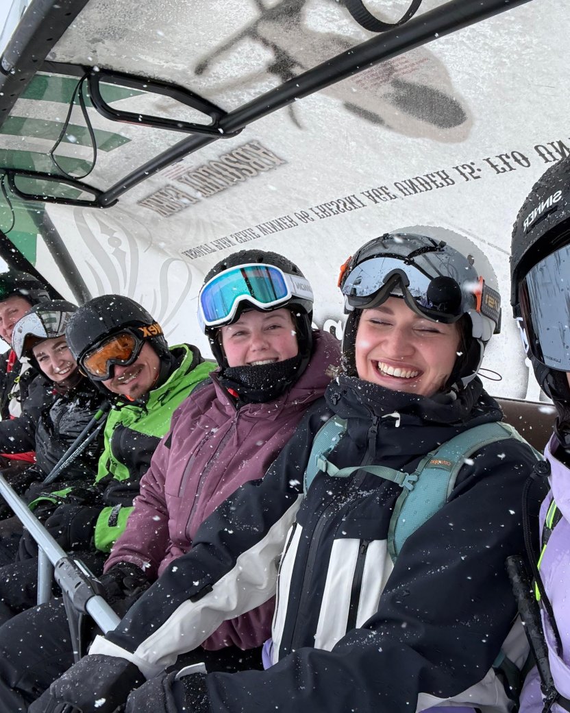 Groep wintersporters zit lachend samen in de stoeltjeslift tijdens een sneeuwbui.