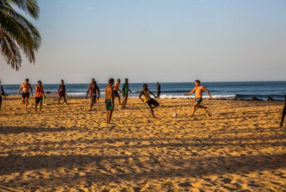 Groep reisgenoten speelt samen voetbal op het strand bij zonsondergang.