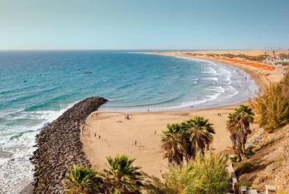 Uitzicht over het strand Playa Del Ingles met blauw water en palmbomen.