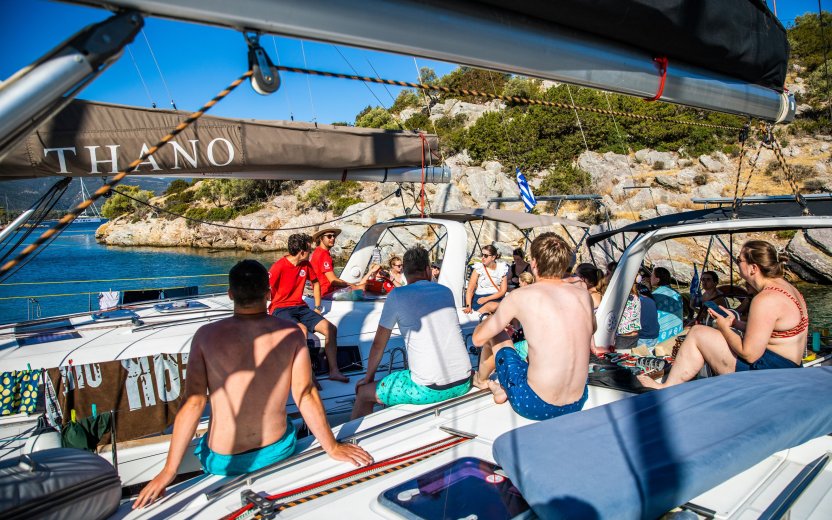 Reisgenoten zitten samen aan boord terwijl de schipper uitleg geeft tijdens de zeiltocht.