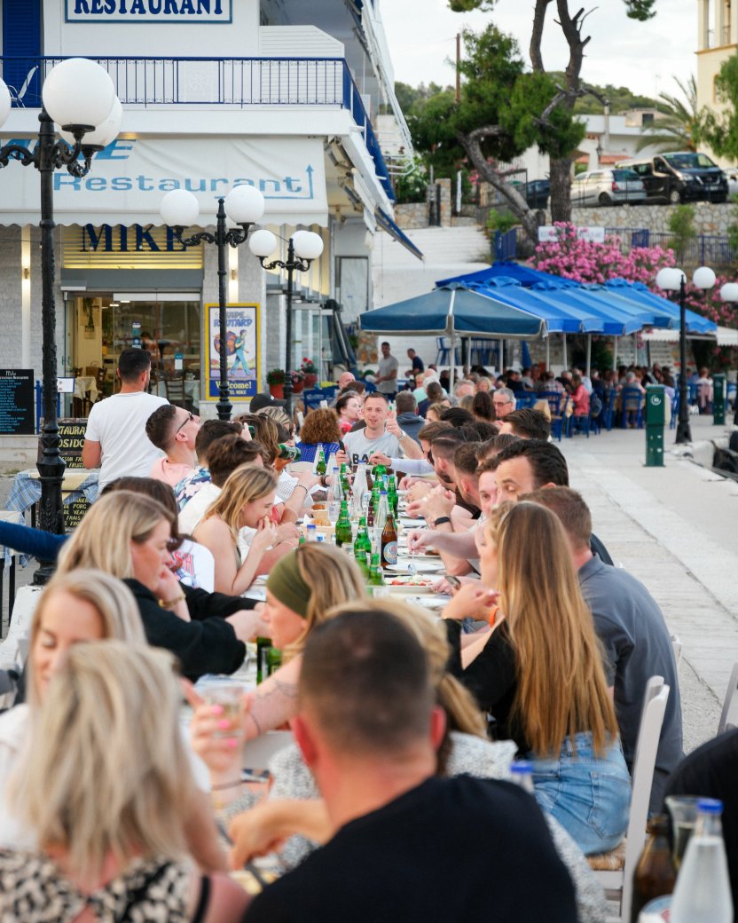 Groep reisgenoten dineert samen aan een lange tafel op een levendig terras.