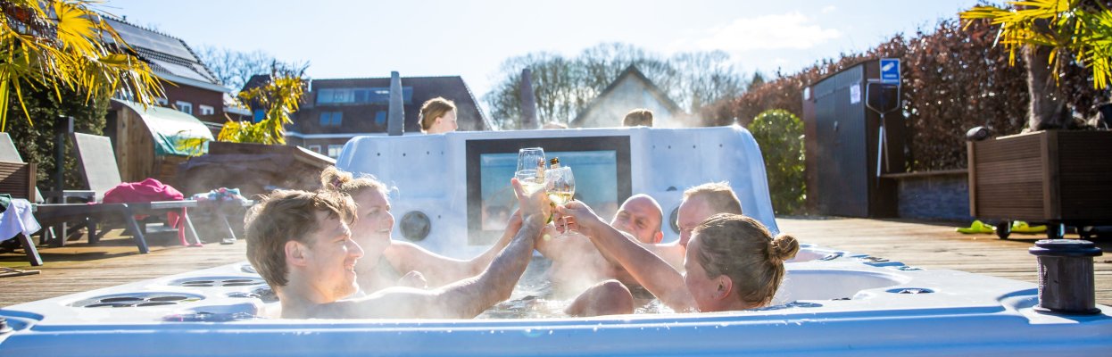 Groep reisgenoten proost samen in een hottub op een zonnig terras.