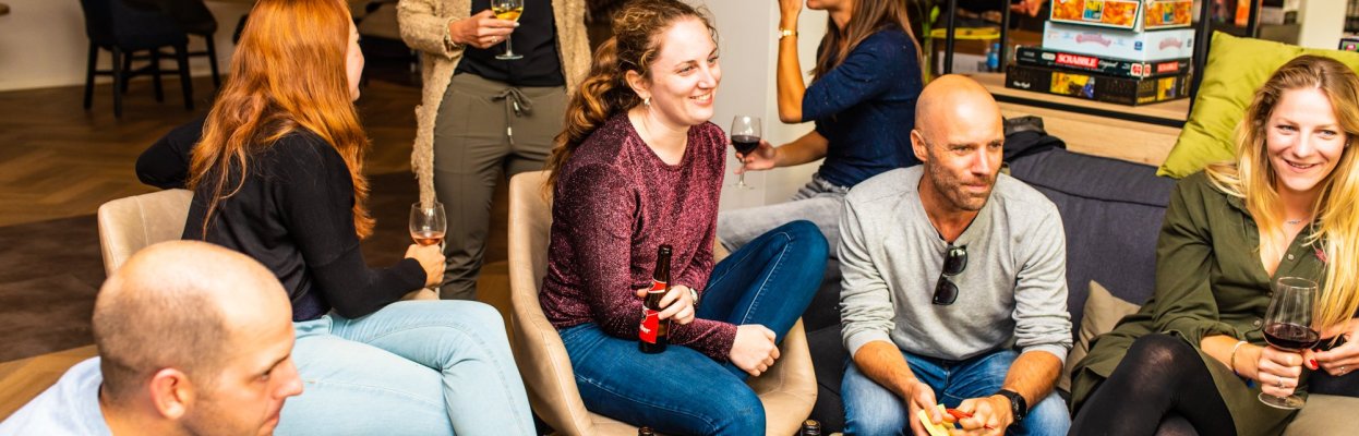 Groep reisgenoten zit samen in de woonkamer met drankjes en hapjes.