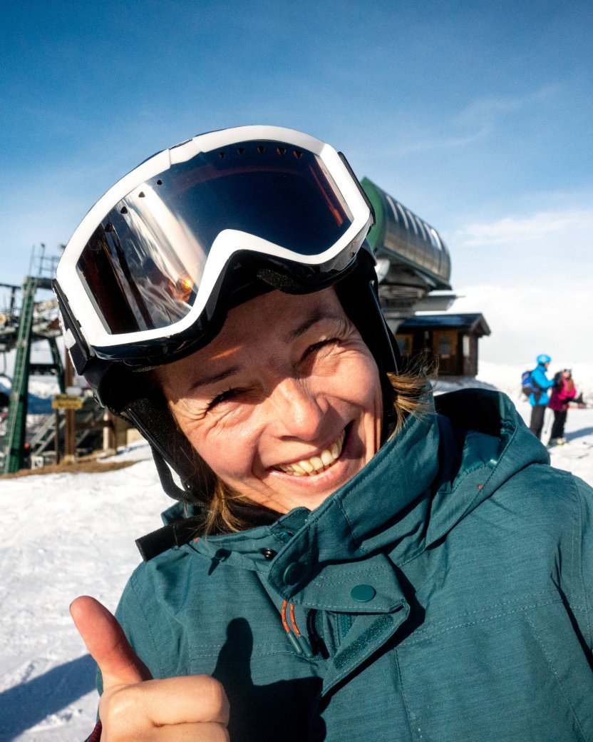 Lachende wintersporter geeft twee duimen omhoog op een zonnige skipiste.