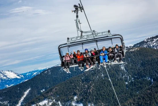 Groep wintersporters samen in de stoeltjeslift met uitzicht op de besneeuwde bergen.