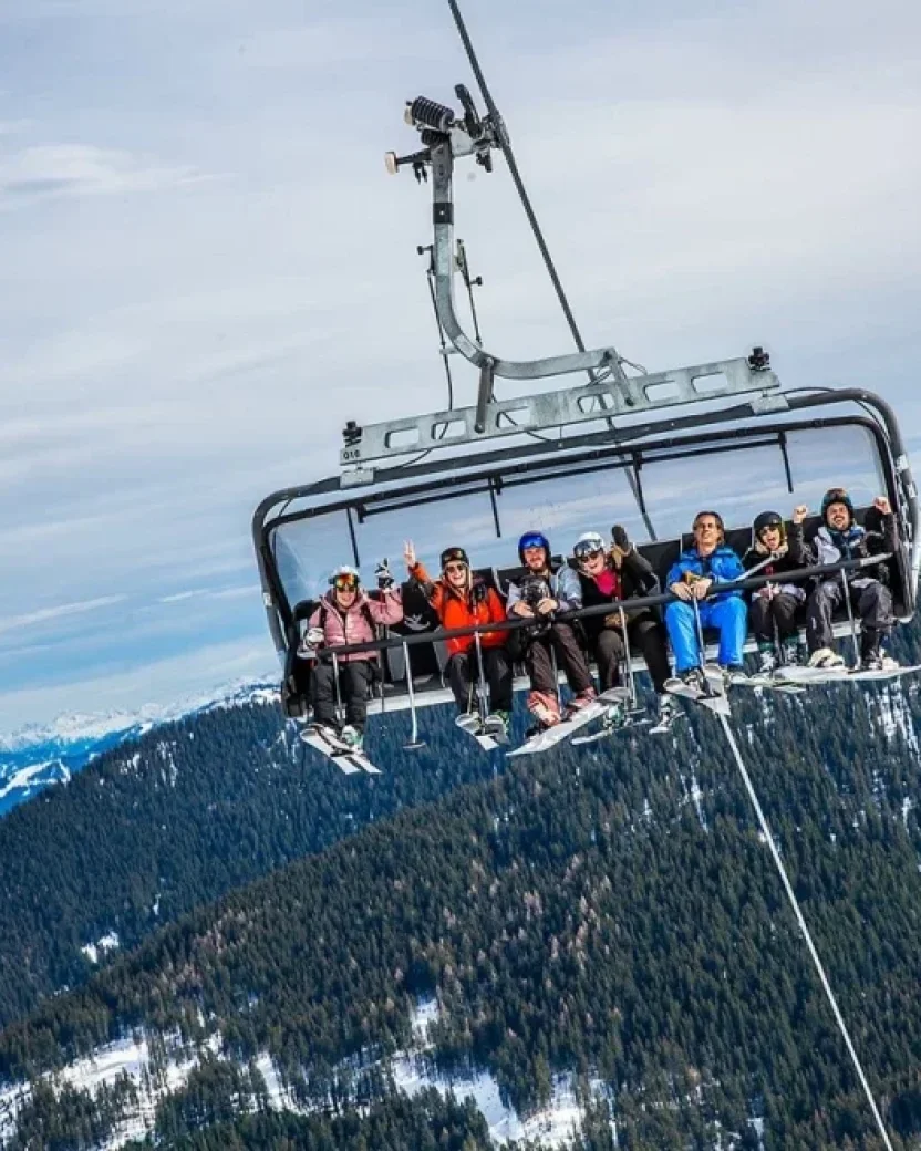 Groep wintersporters samen in de stoeltjeslift met uitzicht op de besneeuwde bergen.