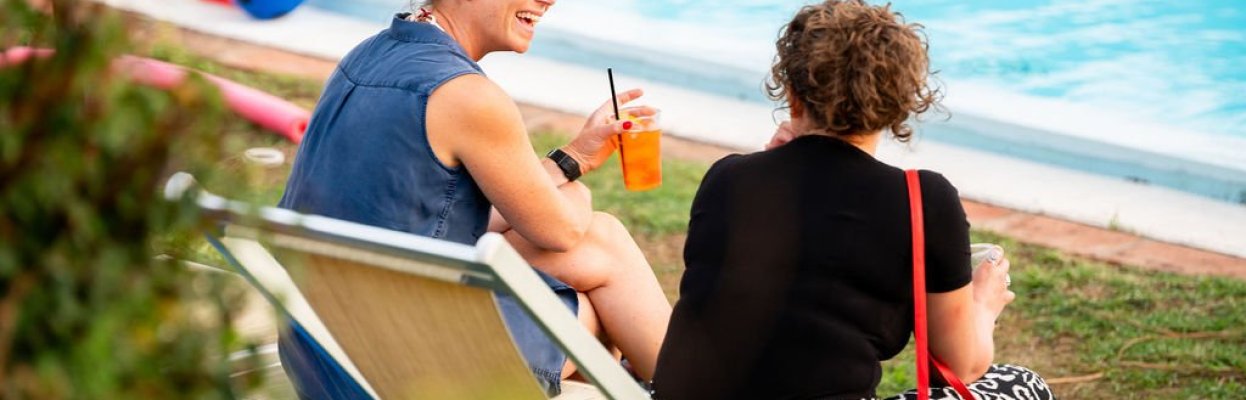 Twee reisgenoten genieten van een drankje naast het zwembad.