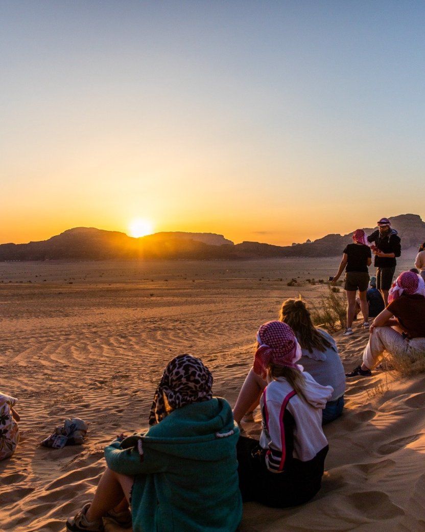 Groep reisgenoten bekijkt de zonsondergang in de woestijn.