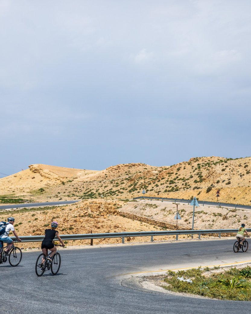 Groep reisgenoten fietst op mountainbikes over de weg door het Jordaanse landschap.