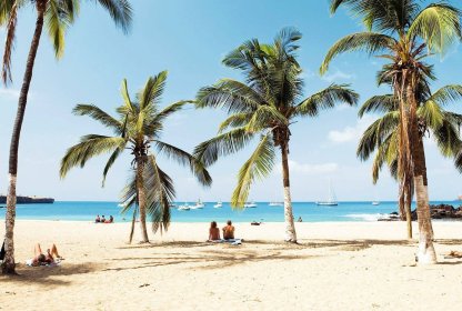 Tropisch zandstrand met palmbomen en zeilboten op het helderblauwe water.